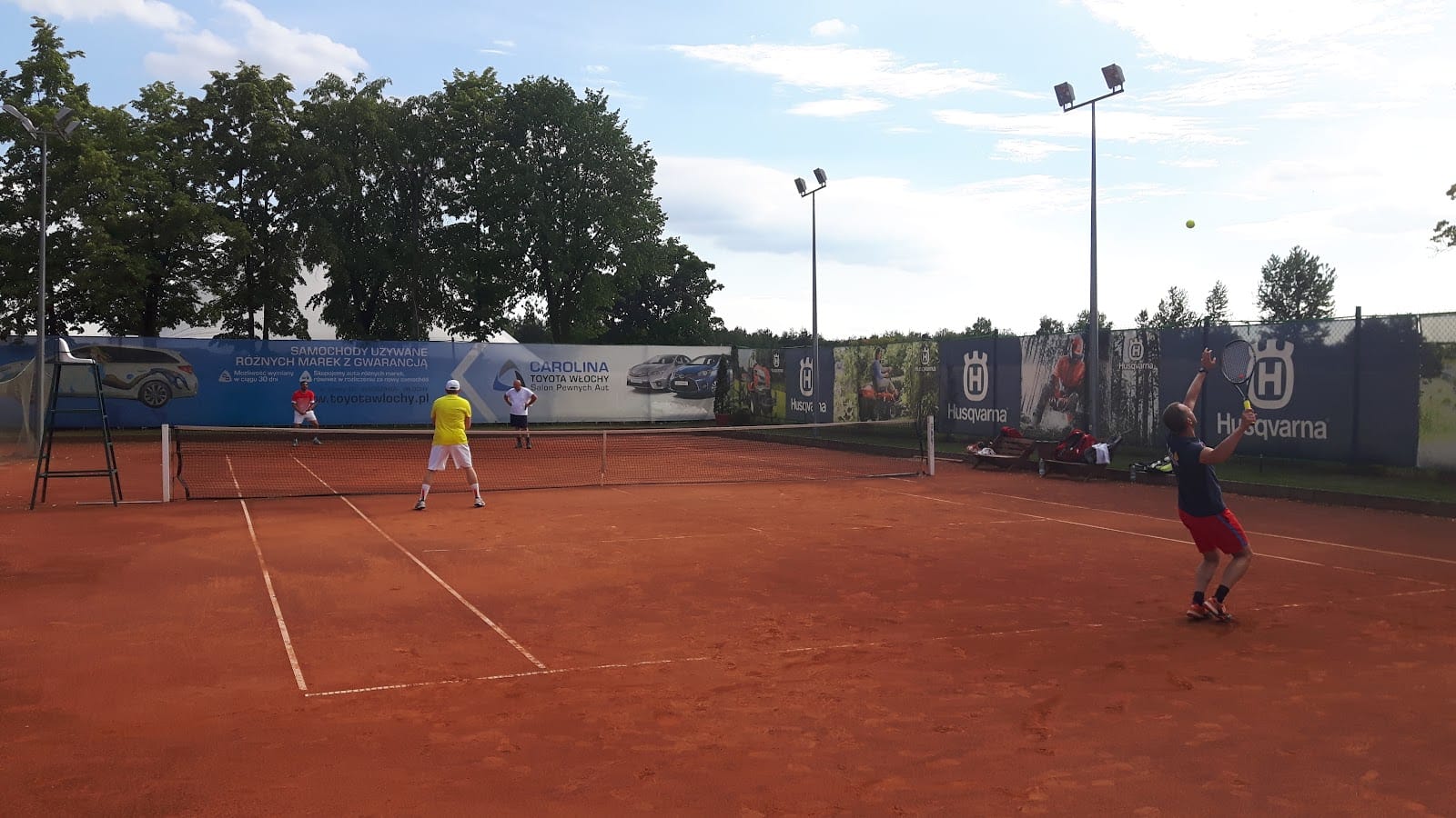Odkryty kort tenisowy z czerwonej mączki w Vamos Tennis Club w Otwocku, gracze podczas meczu w słoneczny dzień