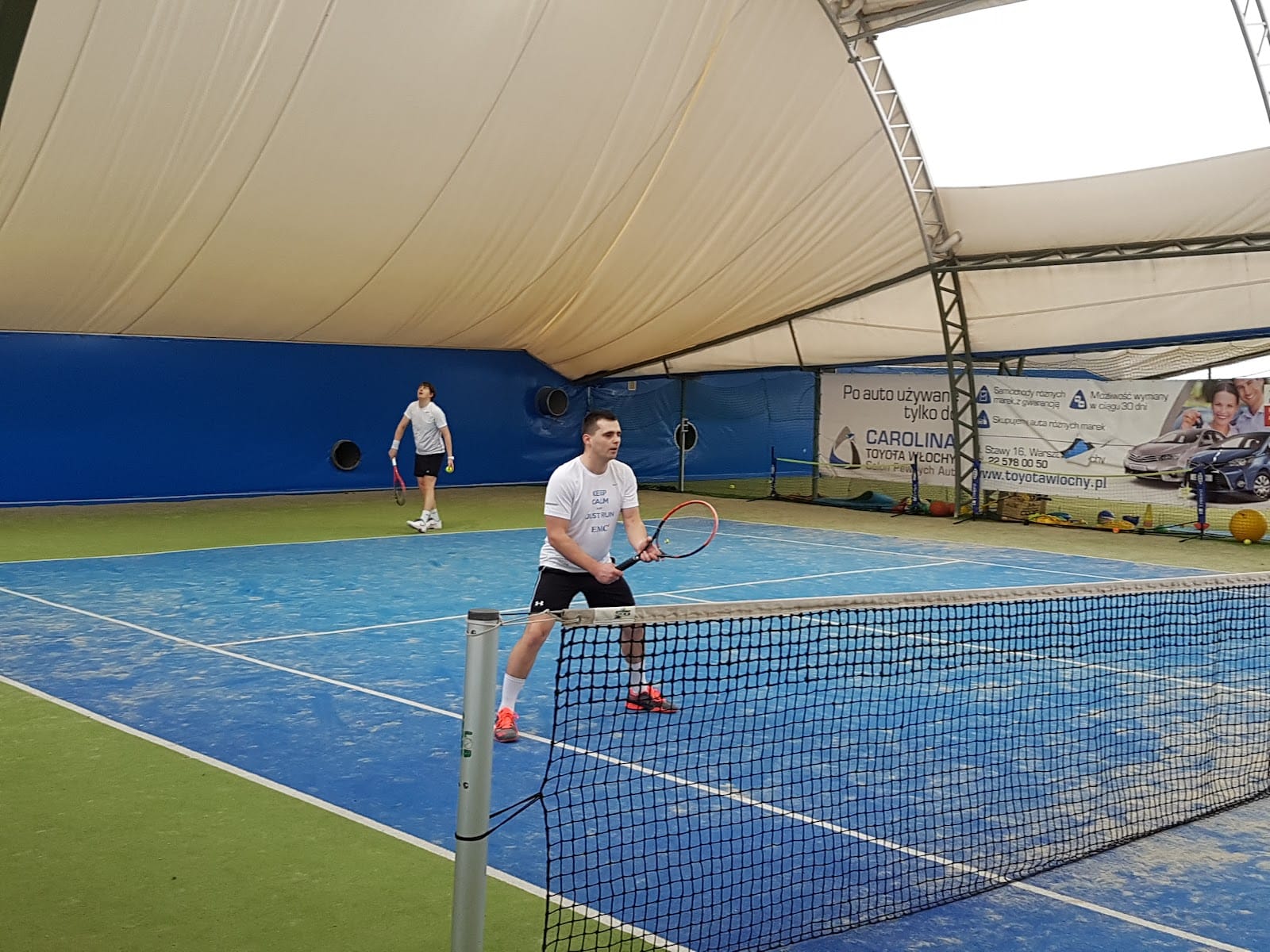 Niebieski kort tenisowy pod ogrzewanym balonem w Vamos Tennis Club, dwóch graczy podczas treningu