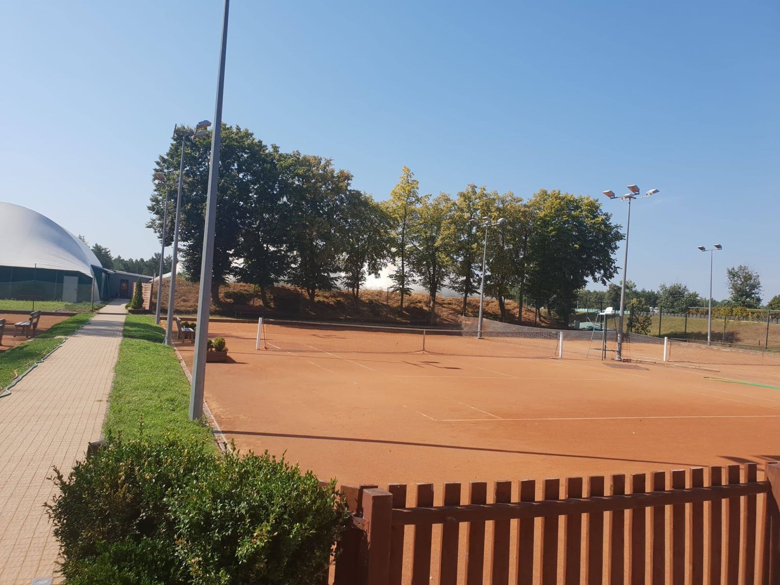 Odkryte korty z mączki w Vamos Tennis Club w słoneczny letni dzień, obok wejście do hali balonowej